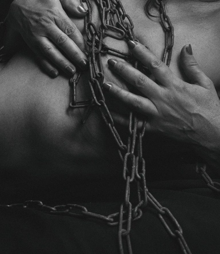 Eine Nahaufnahme von Händen, die über einen mit Ketten umwickelten Oberkörper gleiten.