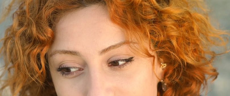 Frau mit lockigem, rotem Haar und einem nachdenklichen Blick.