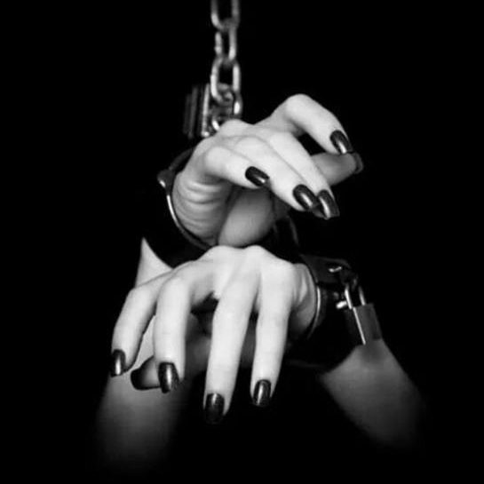 Hände mit schwarzen Nägeln in Handschellen, an einer Kette aufgehängt.
